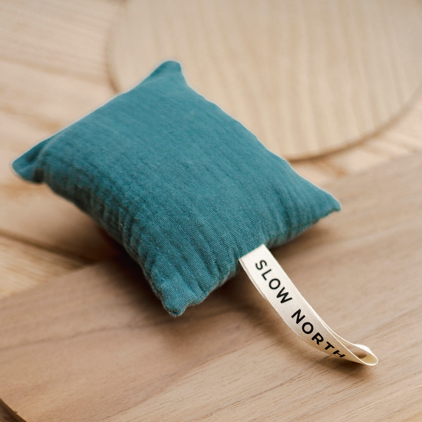 A close-up of a rectangle natural cotton herbal sachet made of teal cotton cloth and filled with cedar chips.