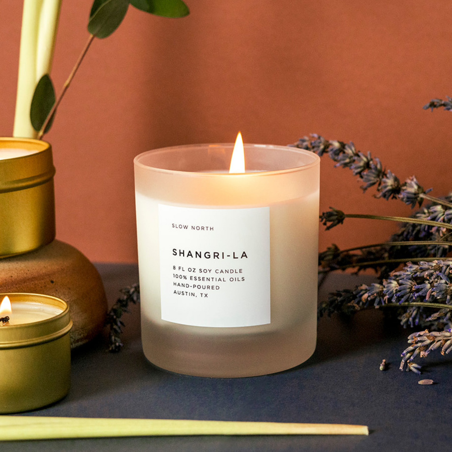 Lit white candle on a dark blue surface in front of a brick red background.